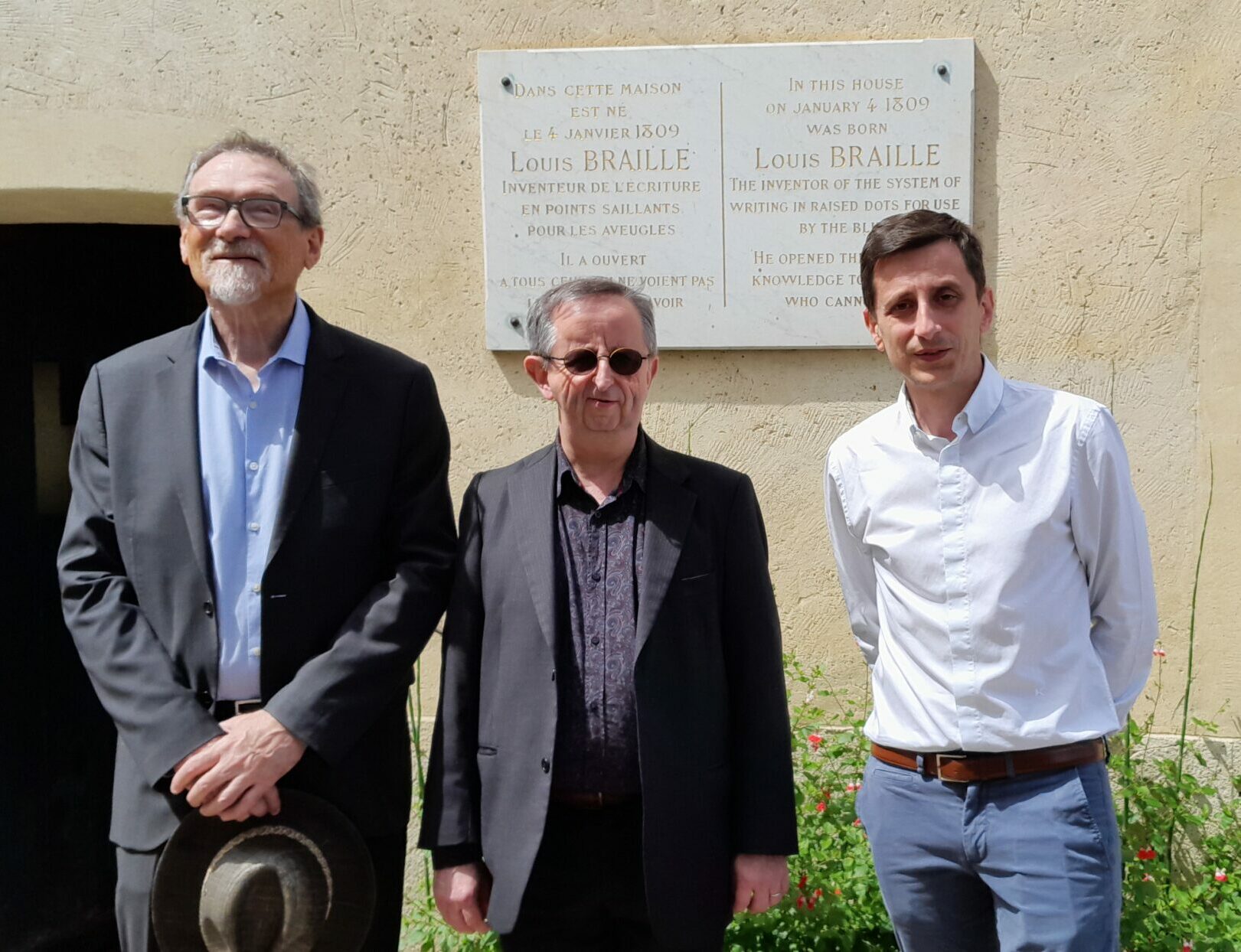 Bruno Gendron Président entouré de Nicolas Blineau directeur général et de Michel Brard secrétaire général, devant la plaque à l’honneur de Louis Braille sur le mur de sa maison natale